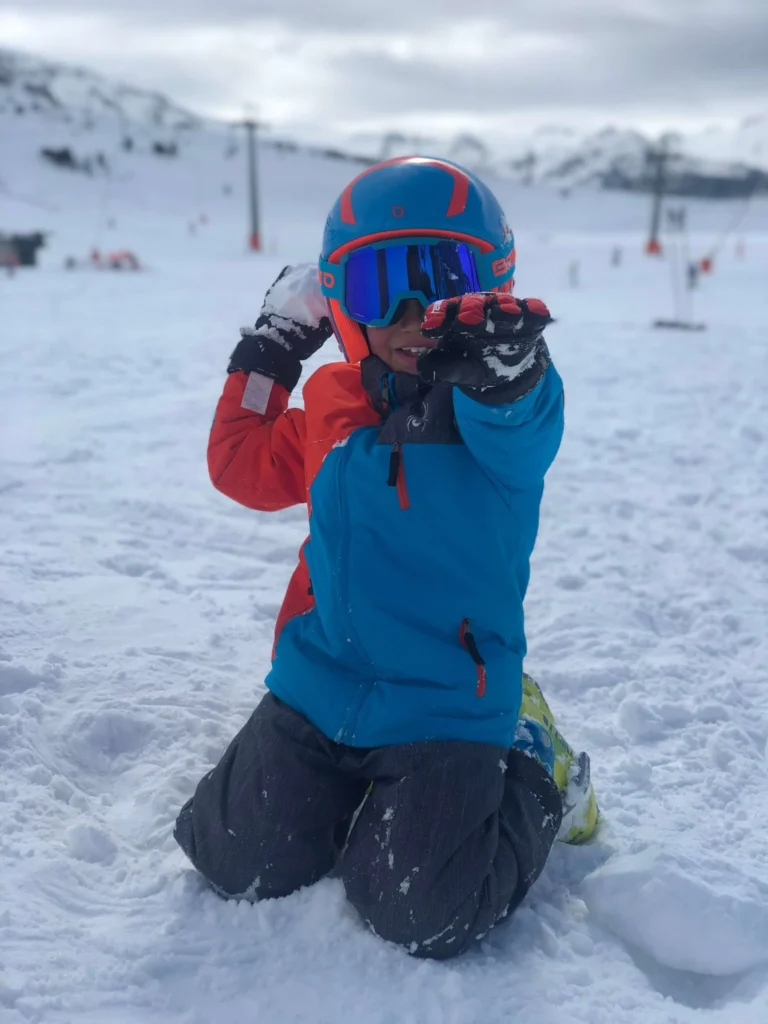 Child skier playing with snowballs wearing a red helmet in Baqueira Beret.
